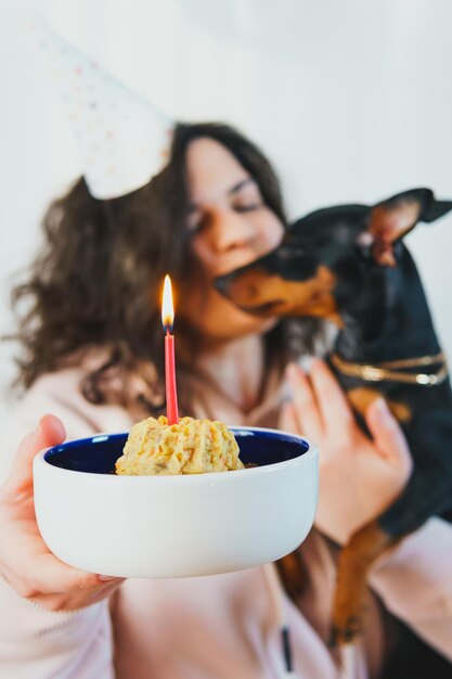 Chica joven feliz dando pastel casero a su perro, en el interior. Concepto de celebrar la fiesta de cumpleaños del perro.