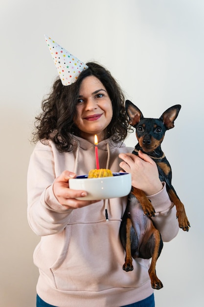 Chica joven feliz dando pastel casero a su perro en el interior