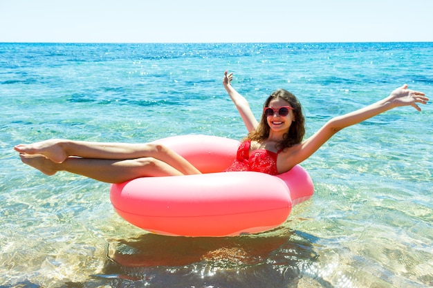 Chica joven feliz en un flotador de donut rociado en el mar sonriendo con gafas de sol para el verano