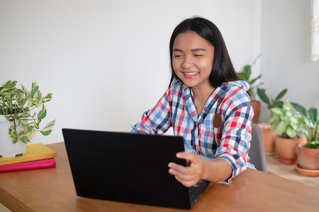 Chica joven feliz que estudia con la computadora portátil en casa