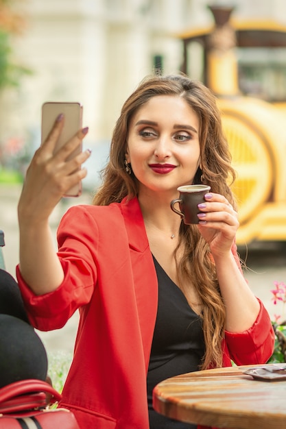 Chica joven feliz que toma el selfie en el café al aire libre.