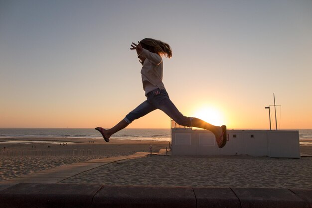 Chica joven feliz saltando en la playa concepto de vacaciones sunsetSummer