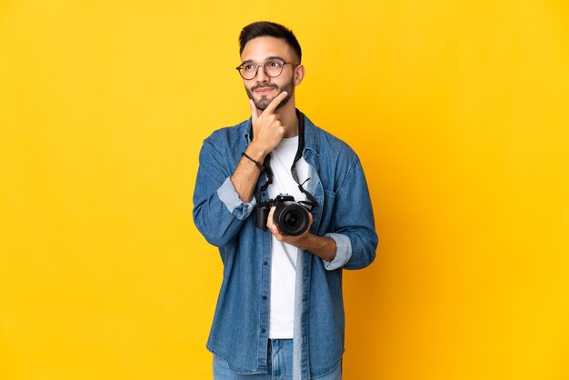 Chica joven fotógrafo aislado sobre fondo amarillo con dudas