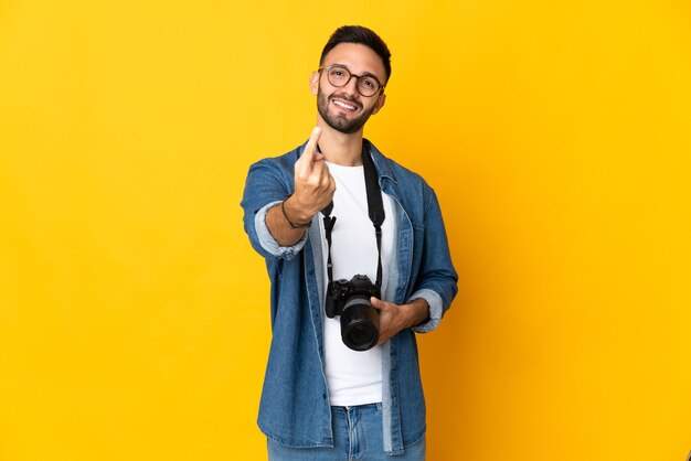 Chica joven fotógrafo aislado sobre fondo amarillo haciendo gesto de venida