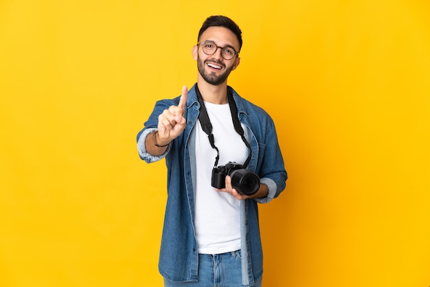 Foto chica joven fotógrafo aislado sobre fondo amarillo mostrando y levantando un dedo