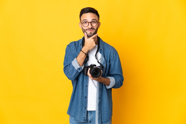 Chica joven fotógrafo aislado sobre fondo amarillo pensando