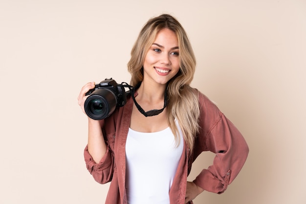 Chica joven fotógrafo sobre pared aislada posando con los brazos en la cadera y sonriendo