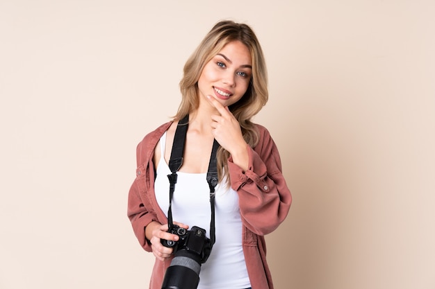 Chica joven fotógrafo sobre pared aislada sonriendo