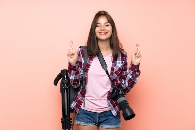 Chica joven fotógrafo sobre pared rosa aislada con cruzar los dedos