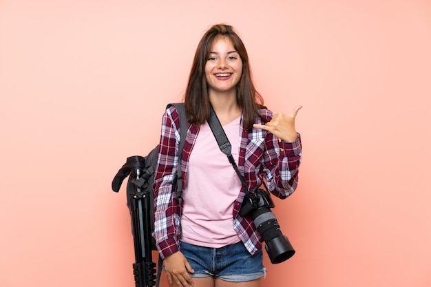 Chica joven fotógrafo sobre pared rosa aislada haciendo gesto de teléfono