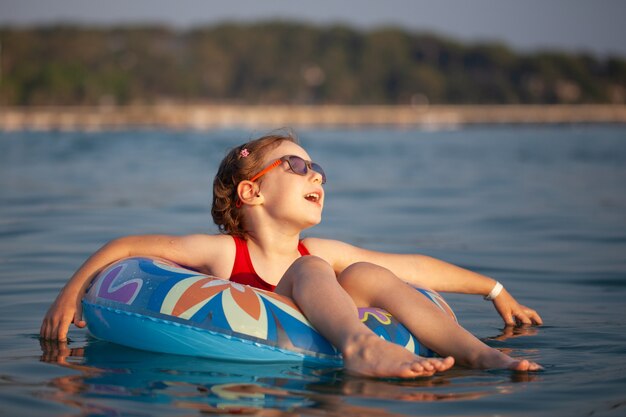 Chica joven con gafas nada en el agua en una rosquilla inflable en el caluroso verano soleado