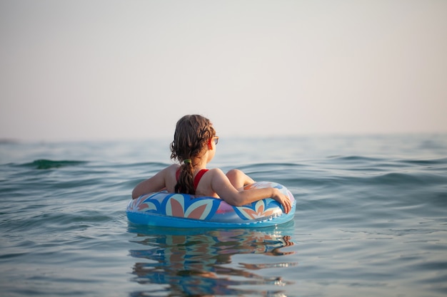 Chica joven con gafas nada en el agua en una rosquilla inflable en el caluroso verano soleado