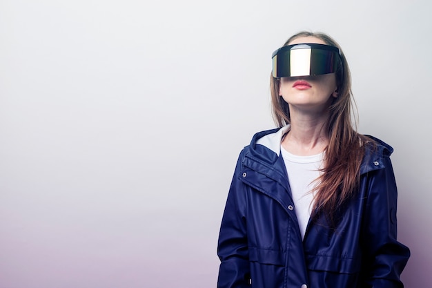 Foto chica joven con gafas de realidad virtual en una chaqueta azul sobre un fondo claro.