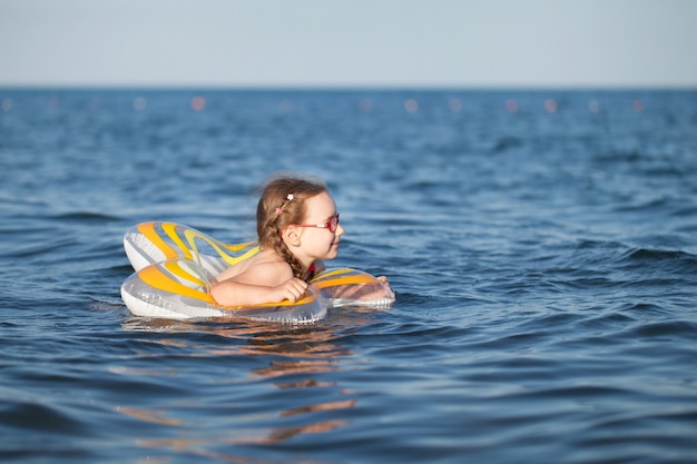 Chica joven con gafas rojas y un traje de baño verde descansando sobre el mar. infancia y aire marino