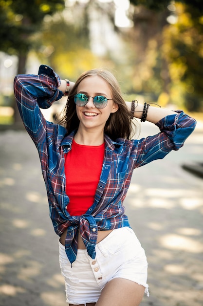 Chica joven con gafas de sol paseando con las manos en la nuca