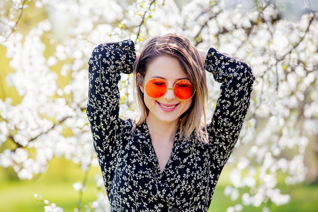 Chica joven en una gafas de sol permanecer cerca de un árbol en flor