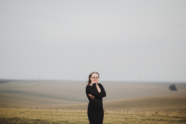 Chica joven con gafas y un vestido negro en un campo