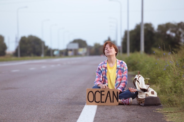 Chica joven con una guitarra que viene a lo largo del camino y que hace autostop