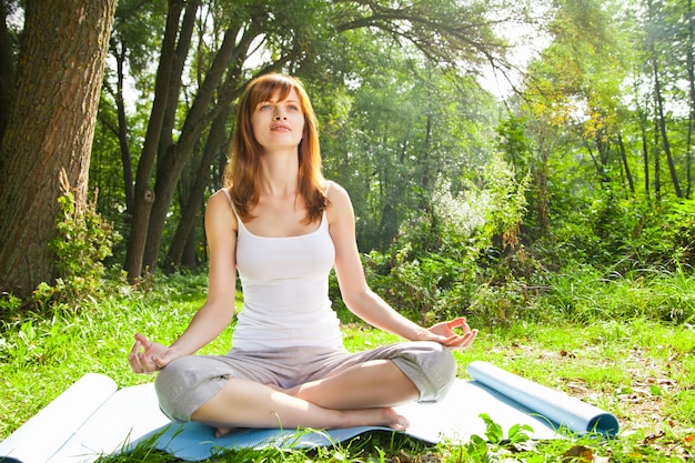 Foto chica joven haciendo pose de loto de yoga en el parque