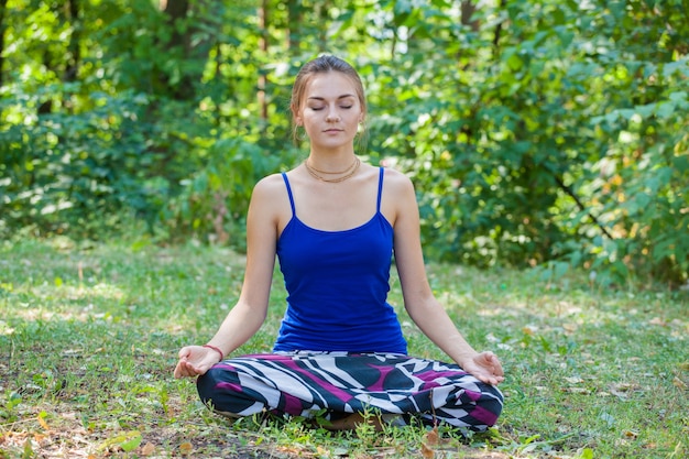 Chica joven haciendo yoga en el parque sobre la hierba