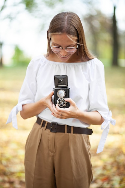 Chica joven hermosa atractiva que sostiene la cámara retro de la reflexión de la lente doble del vintage en el parque del otoño