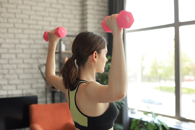 Chica joven hermosa deportes en leggings y un top hace ejercicios con pesas. Estilo de vida saludable. Una mujer practica deportes en casa.