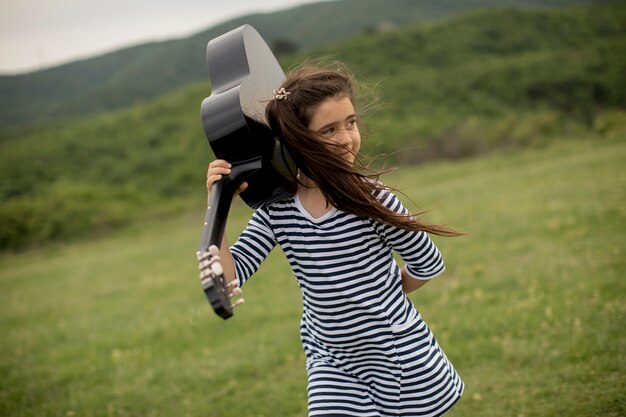 Chica joven hermosa que lleva su guitarra en naturaleza