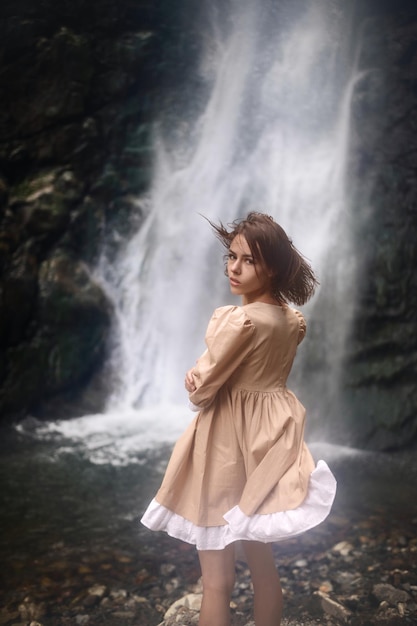 Chica joven hermosa en un vestido en el fondo de una cascada