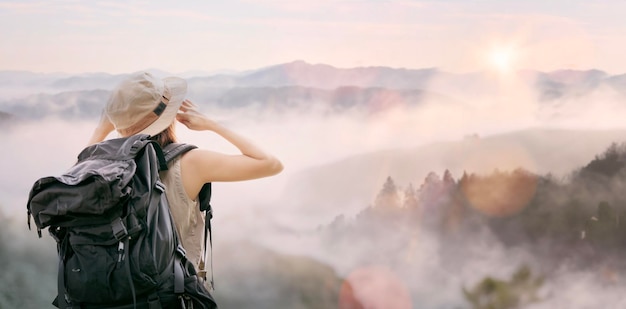 Chica joven hipster con mochila disfrutando del atardecer en la cima de la montaña brumosa