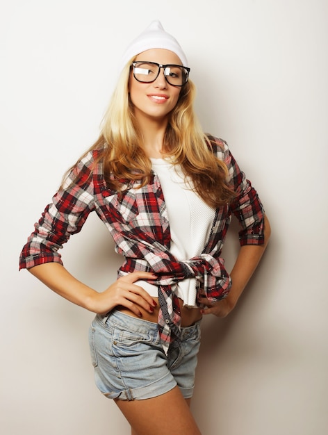 Chica joven inconformista divirtiéndose y volviéndose loca, con sombrero de gafas y maquillaje brillante. Fondo blanco.