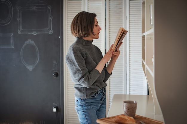 Chica joven inconformista está leyendo un libro en casa. Entrenamiento, estudiante se prepara para el examen. libro antiguo rareza antigüedades. Espacio libre. Tablero revestido con marcos. Lugar para el diseño del texto