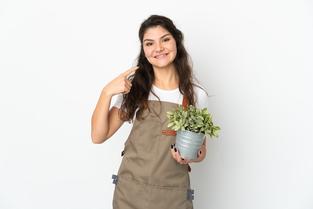 Chica joven jardinero ruso sosteniendo una planta aislada dando un pulgar hacia arriba gesto