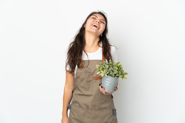 Chica joven jardinero ruso sosteniendo una planta riendo aislado