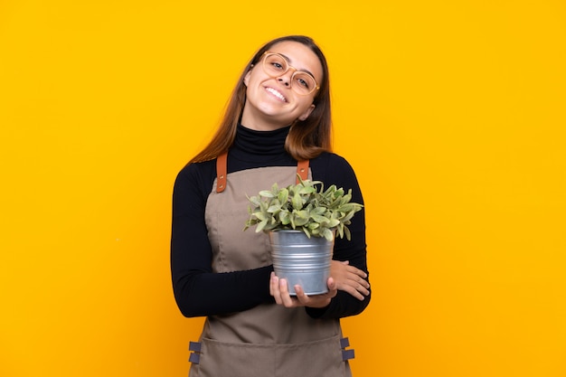 Chica joven jardinero sosteniendo una planta sobre risa amarilla aislada