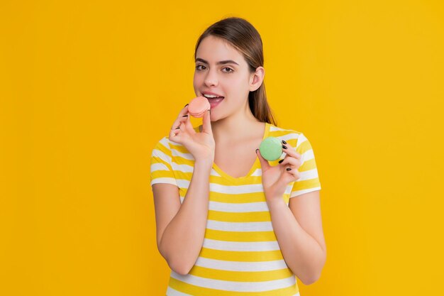 Chica joven lamiendo macaron sobre fondo amarillo