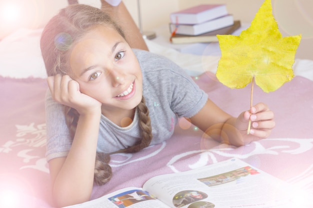 Chica joven con el libro y la hoja amarilla del otoño