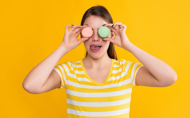 Chica joven con macaron lamiendo labios sobre fondo amarillo