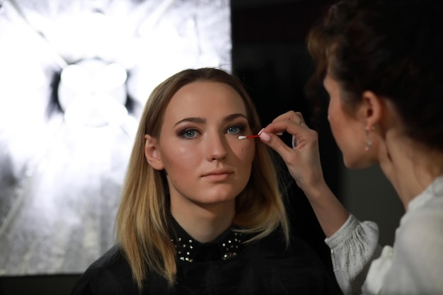 Chica joven con un maquillador en el estudio frente a un espejo