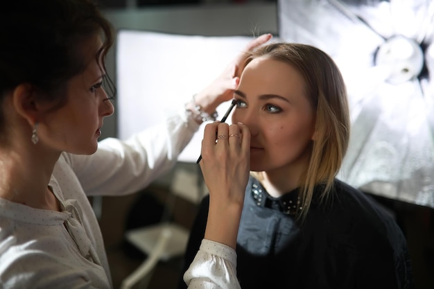 Chica joven con un maquillador en el estudio frente a un espejo