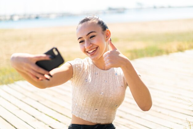 Chica joven marroquí al aire libre haciendo un selfie con teléfono móvil