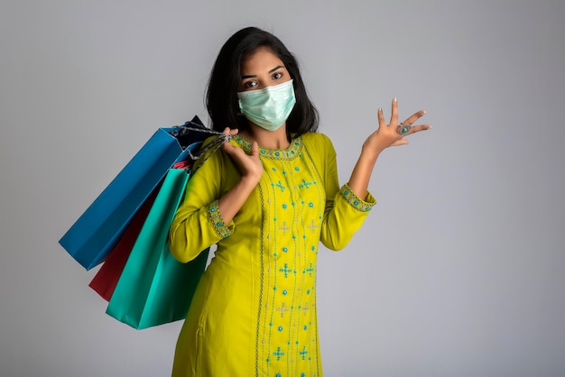 Chica joven con máscara médica sosteniendo bolsas de compras sobre fondo gris. Concepto de venta de descuento comercial.