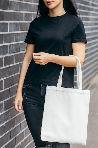 Chica joven modelo asiática vestida con una camiseta blanca en la calle sosteniendo una bolsa ecológica blanca simulada