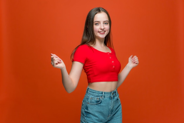 Chica joven moderna y alegre bailando moviendo las manos divirtiéndose disfrutando de la música en el estudio naranja