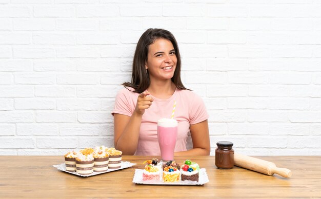 Chica joven con un montón de diferentes mini tortas te señala con el dedo