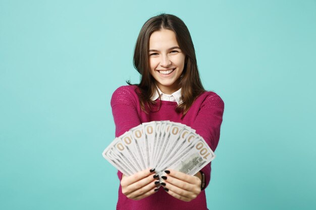 Chica joven morena con ropa informal posando aislada en un retrato de estudio de fondo azul. Concepto de estilo de vida de las emociones de las personas. Simulacros de espacio de copia Sostenga en la mano abanico de dinero en efectivo en billetes de dólar