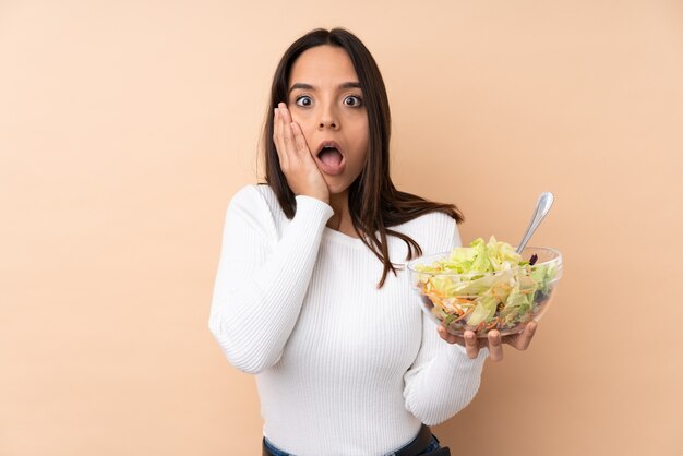 Chica joven morena sosteniendo una ensalada aislada