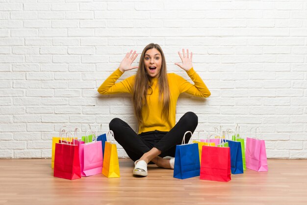 Chica joven con muchas bolsas de compras con sorpresa y expresión facial conmocionada