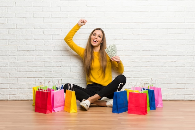 Chica joven con muchas bolsas de compras tomando mucho dinero