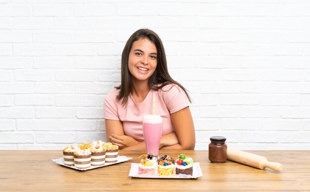 Chica joven con muchos mini pasteles diferentes riendo