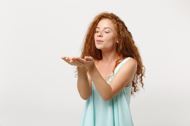 Chica joven mujer pelirroja muy sonriente en ropa ligera casual posando aislada sobre fondo blanco en estudio. Concepto de estilo de vida de emociones sinceras de personas. Simulacros de espacio de copia. Soplando enviando beso al aire.